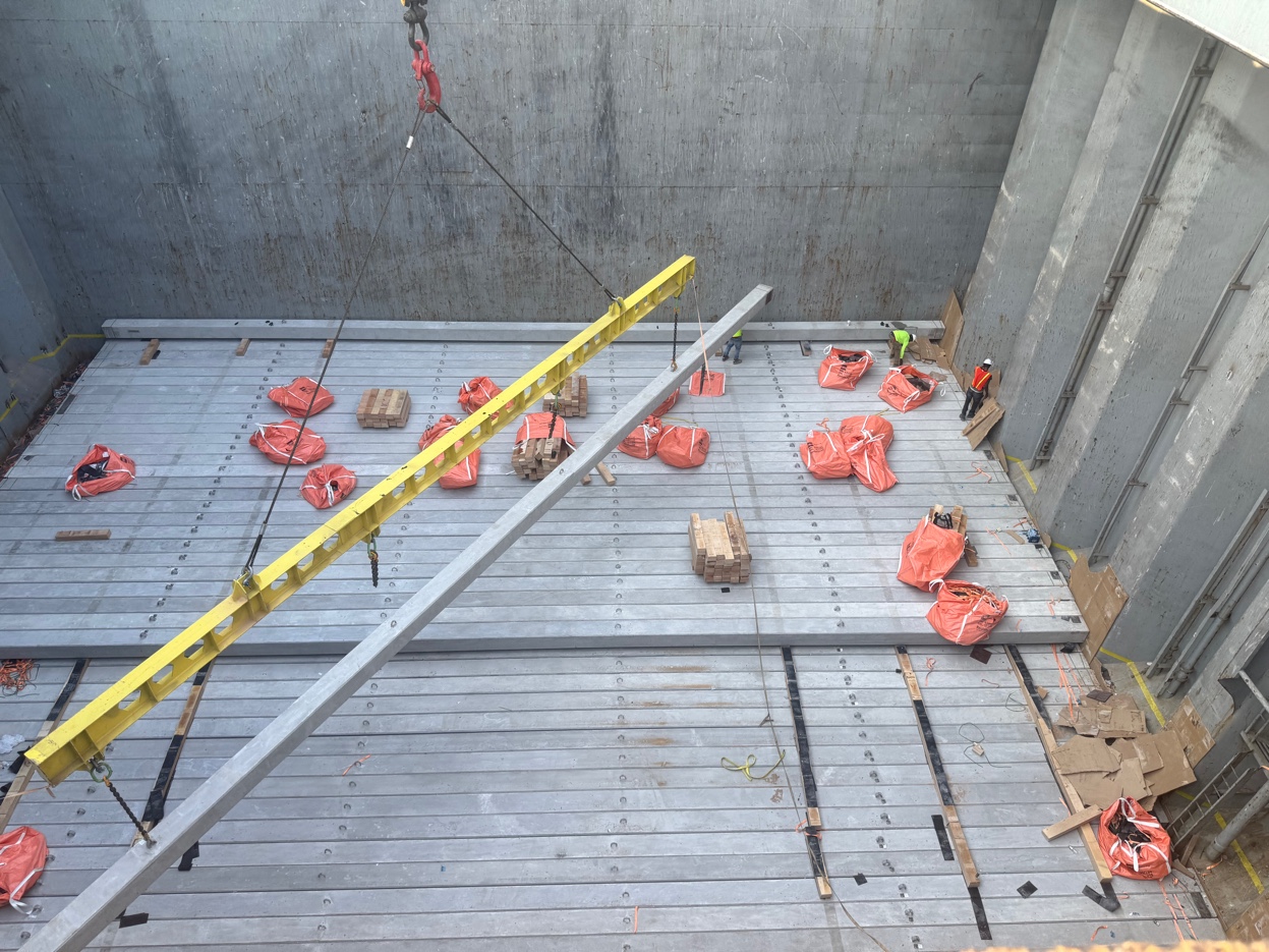 Looking down into ship hold during GCS concrete pile discharge operation — 90-foot piles, rigging bags, and workers visible below